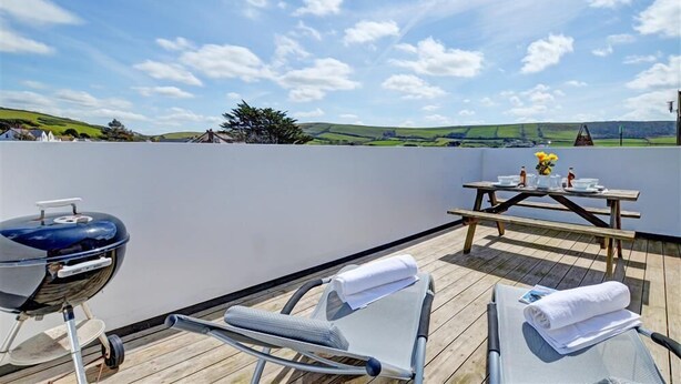 Une terrasse sur le toit équipée d’un barbecue, de chaises longues et d’une table offrant une vue sur la campagne.