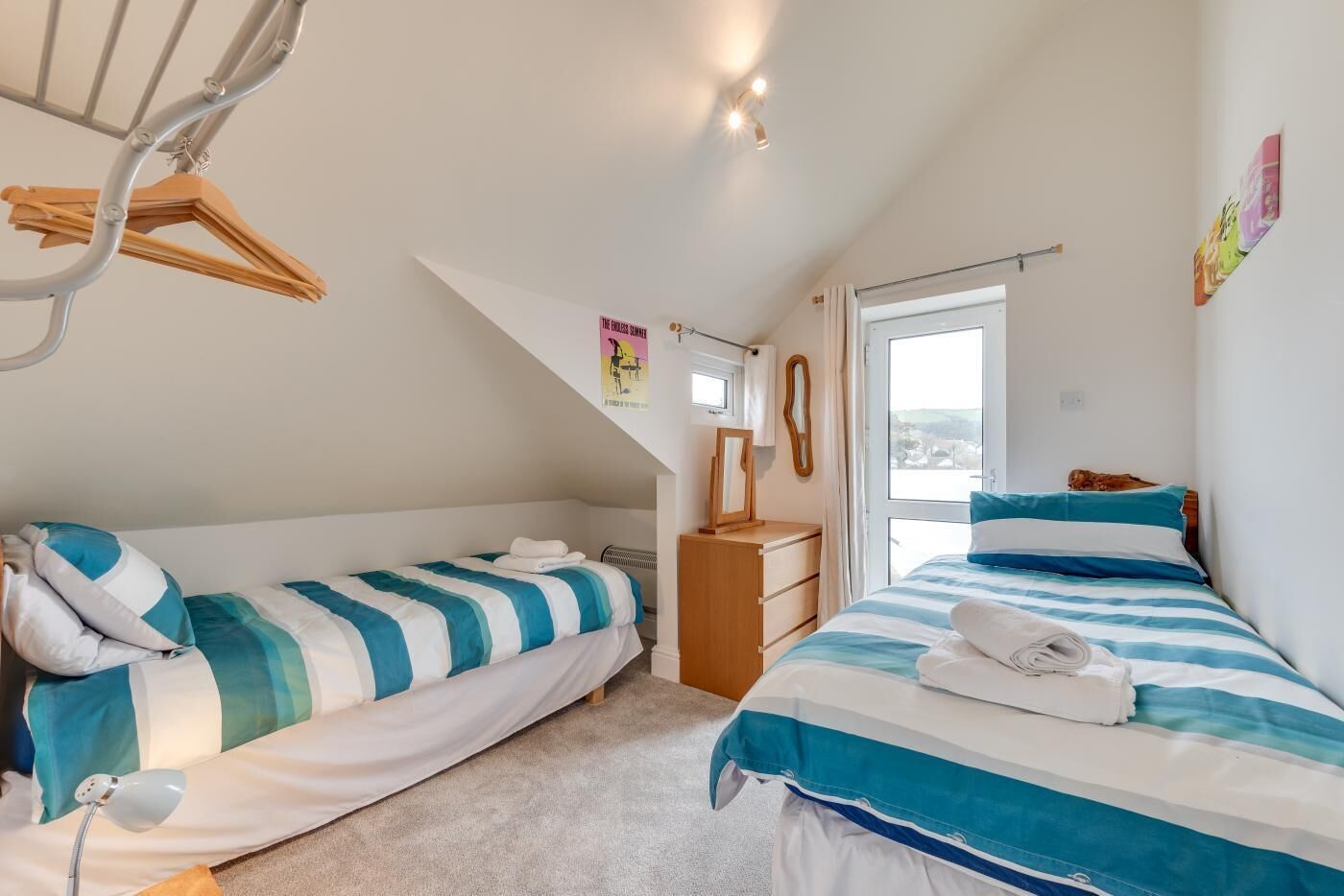 A bedroom with two beds, a dresser, a mirror, and a hanging clothes rack.