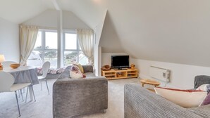 Un salon chaleureux de style loft, doté d’une grande fenêtre, d’un téléviseur à écran plat et d’un coin repas avec une table et des chaises.