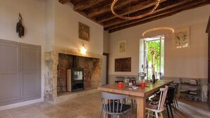 A rustic dining area with a brick fireplace, wooden ceiling beams, and a large wooden table with chairs.