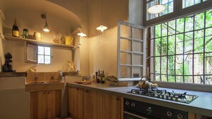 A kitchen with wooden cabinets, a gas stove, an oven, a window with a view of greenery, and various kitchen items on the countertop.