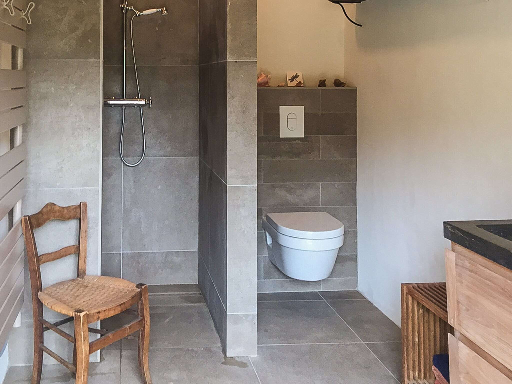 Un baño con ducha, inodoro y una silla de madera.