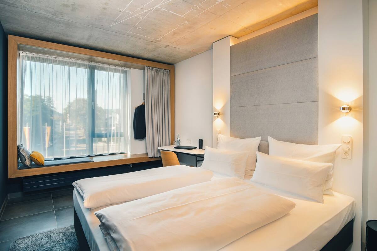 A modern hotel room with a large bed, a desk, and a window with curtains.