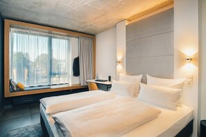 A modern hotel room with a large bed, a desk, and a window with curtains.