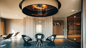 A modern interior with a round ceiling light, dark tiled floor, and three black chairs with white cushions. - VILOTEL - Hotel & Restaurant (Oberkochen)
