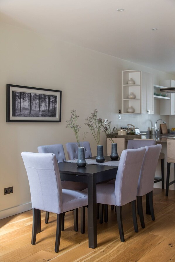 A dining area with a black table, six grey upholstered chairs, and three vases with plants.