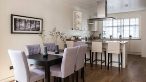 A modern kitchen with a dining area, featuring a black dining table, grey upholstered chairs, and a kitchen island with a sink and stove. - Campden Street VI by onefinestay (London)
