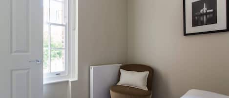 Un dormitorio con una cama, un radiador, una silla, una puerta y un cuadro en la pared.
