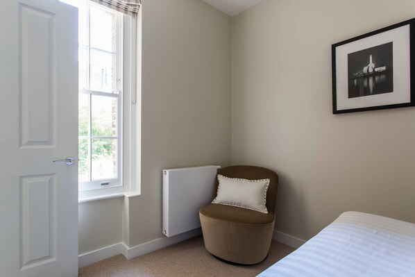 A bedroom with a bed, a radiator, a chair, a door, and a framed picture on the wall.