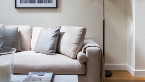 A modern living room with a sofa, a floor lamp, a framed picture on the wall, and a coffee table with books and a glass. - Campden Street VI by onefinestay (London)