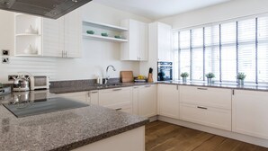 A modern kitchen with white cabinetry, granite countertops, and a built-in stove. - Campden Street VI by onefinestay (London)