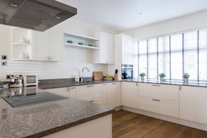 A modern kitchen with white cabinetry, granite countertops, and a built-in stove. - Campden Street VI by onefinestay (London)