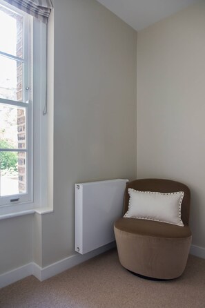 A corner room with a radiator, a window, and a brown chair with a white cushion.