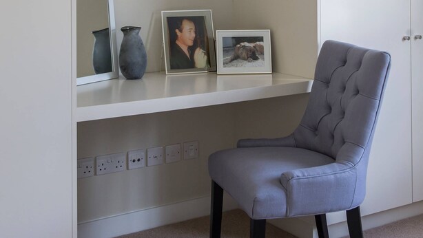 A room with a white desk, a grey chair, and a shelf with a vase, a framed photo, and a picture frame. - Campden Street VI by onefinestay (London)