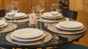 A dining table set with plates, glasses, and cutlery, surrounded by wooden cabinets and a kitchen area. - Abbey Apartments City Center I Bolhão Market (Porto)
