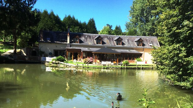 A lakeside building with a dining area and a duck swimming in the water. - Le Moulin Calme (Luceau)
