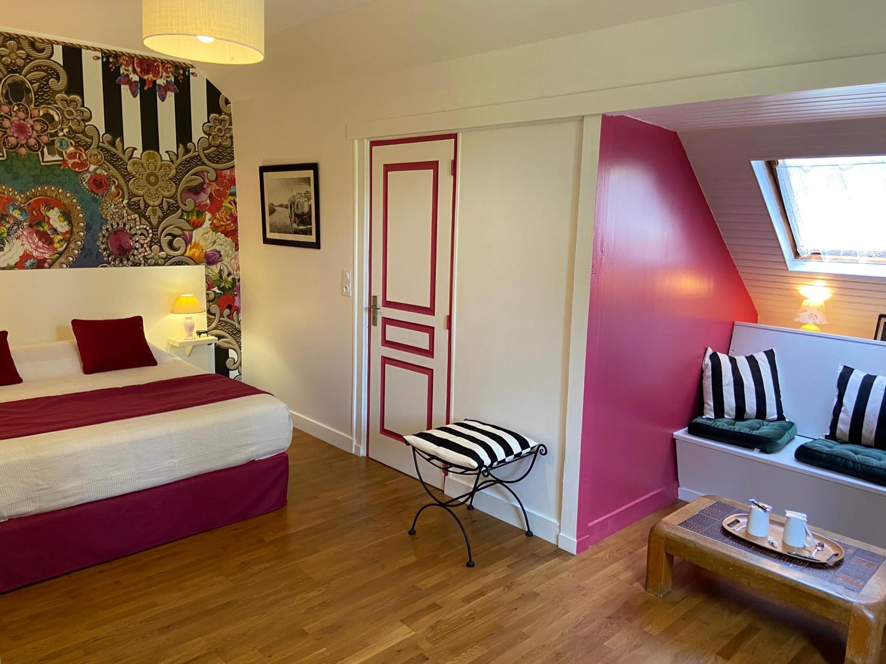 A bedroom with a bed, a chair, a small table with cups, a door, and a window.