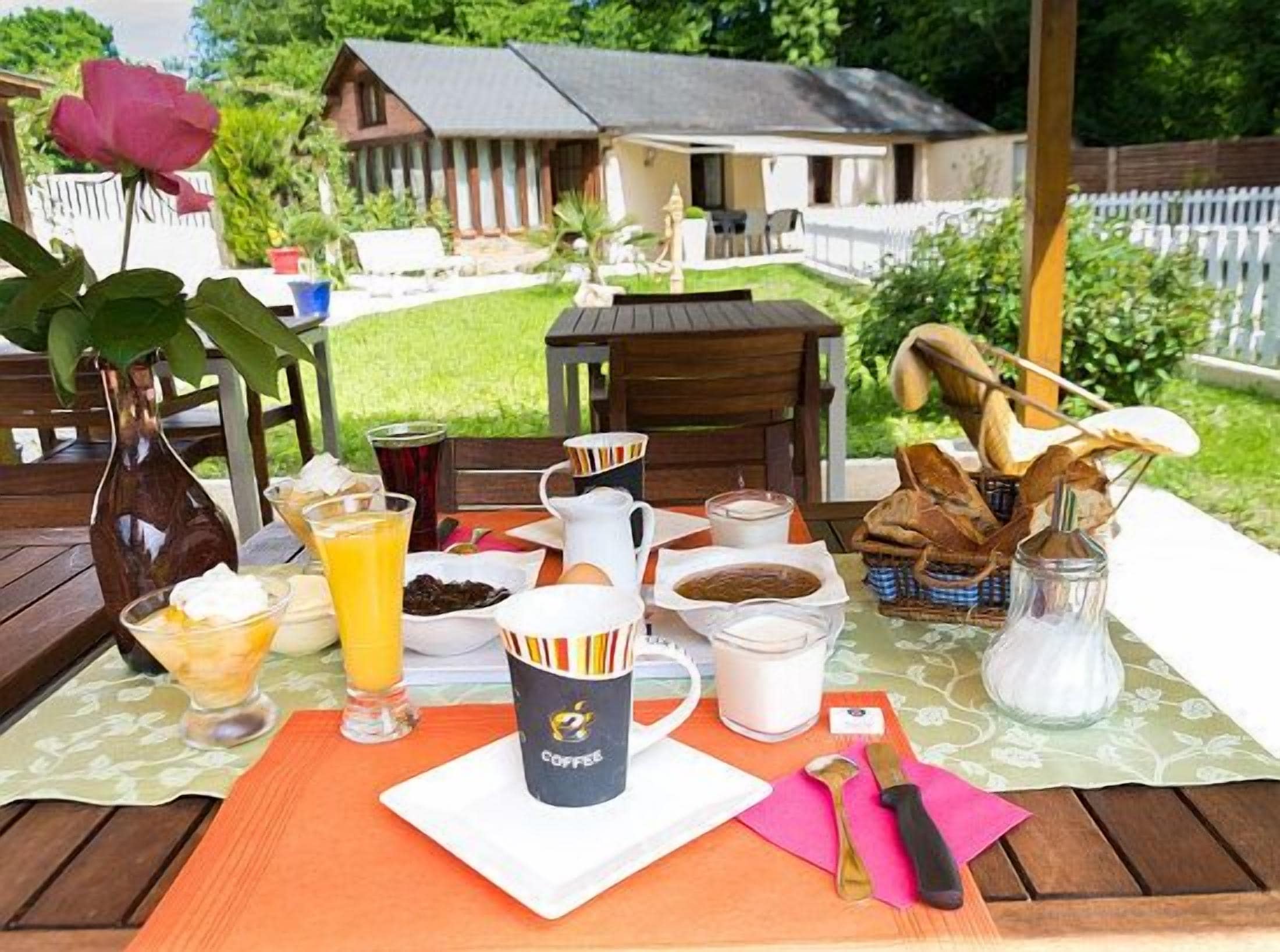 A breakfast setup on an outdoor table with a view of a house and garden.