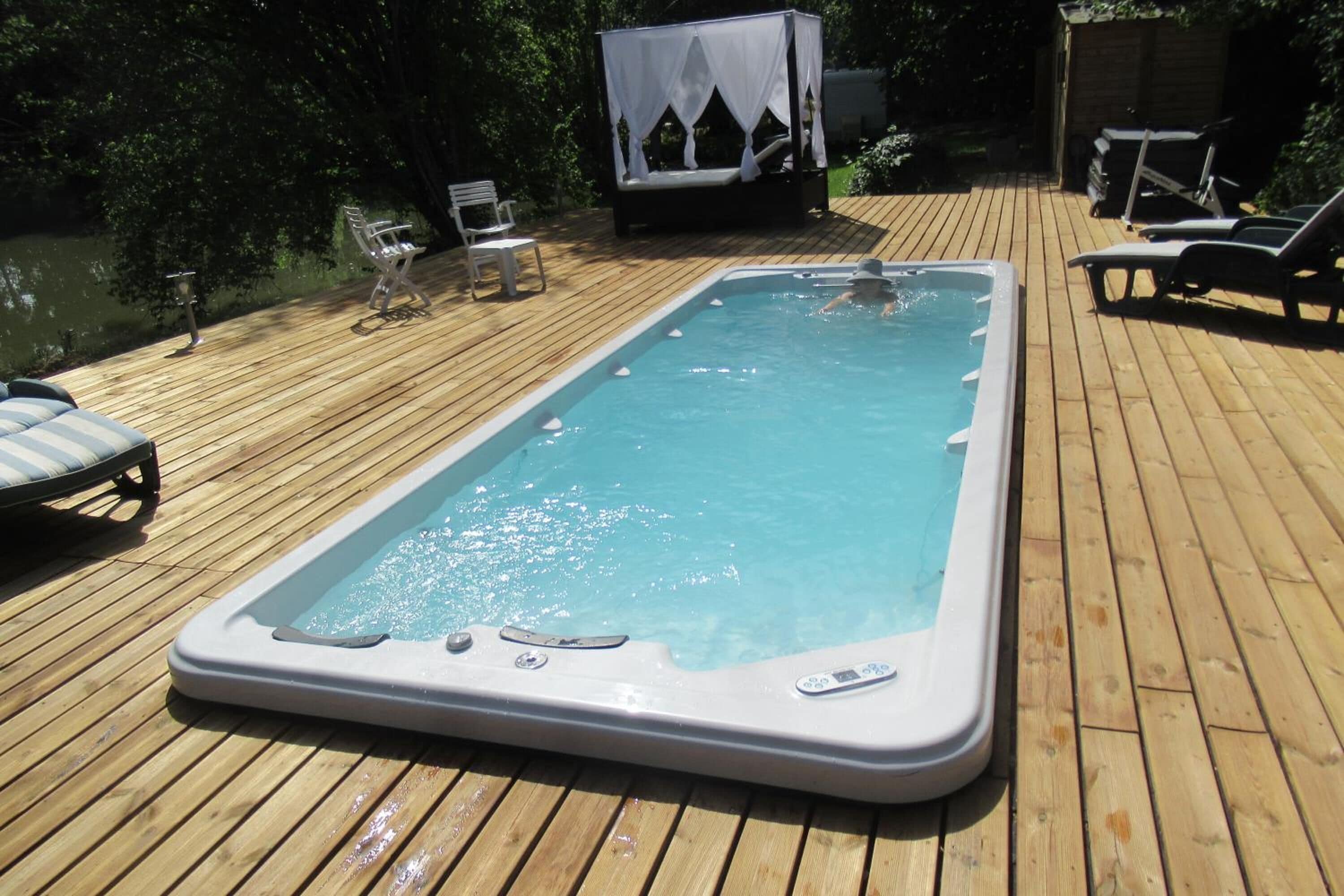 A hot tub on a wooden deck with lounge chairs and a canopy.