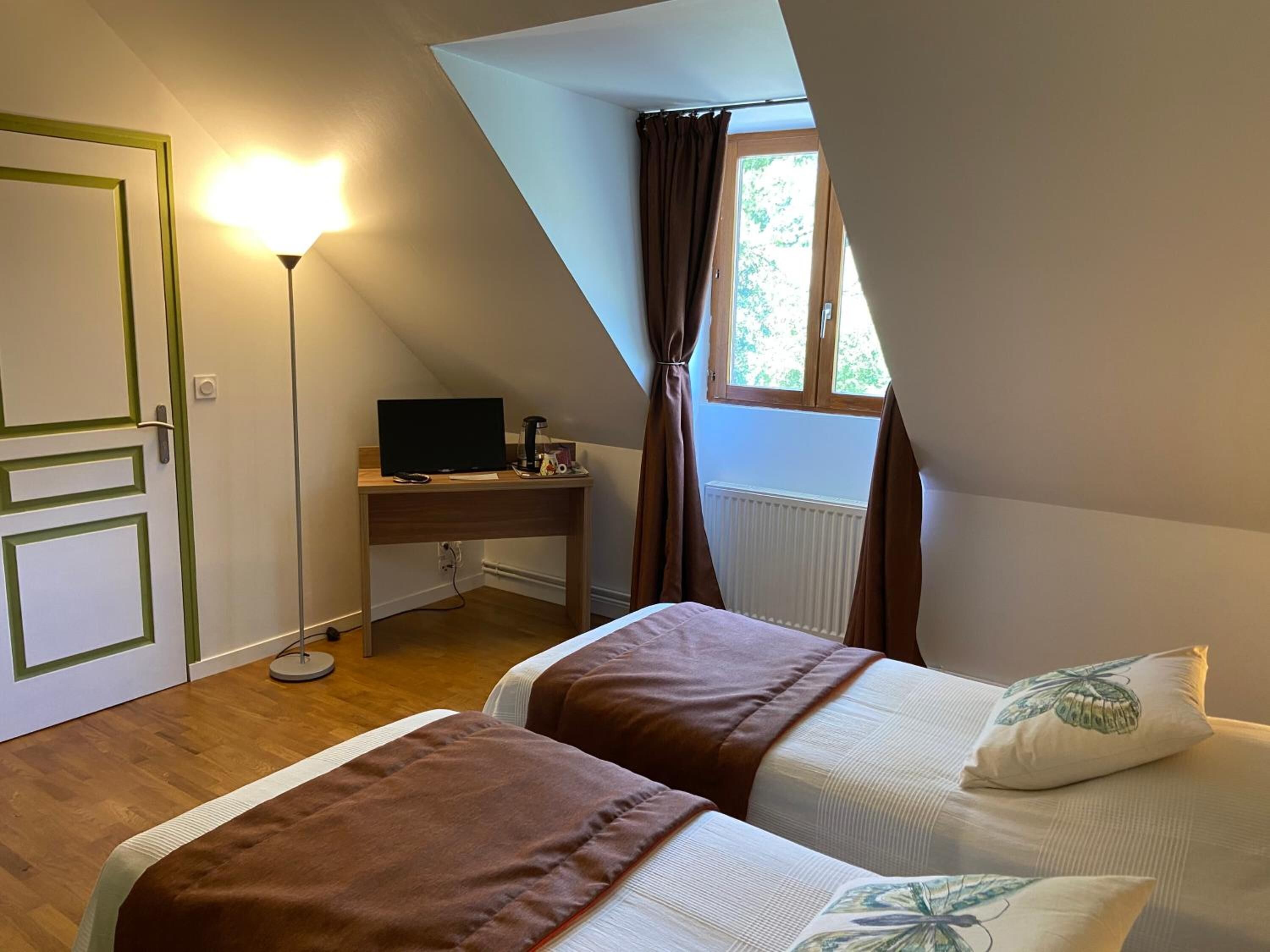 A bedroom with two beds, a desk, a computer, and a window with curtains.