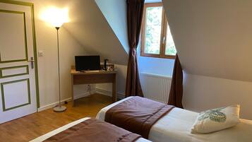 A bedroom with two beds, a desk, a computer, and a window with curtains.