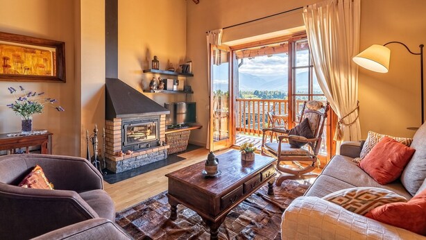Una sala de estar acogedora con chimenea, asientos cómodos y un balcón con vistas panorámicas.