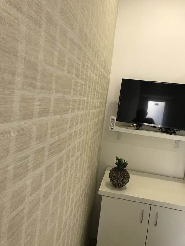 A room with a patterned wall, a flat-screen TV mounted on a shelf, and a small cabinet with a pineapple decoration. - Terrazza Aragon (Naples)