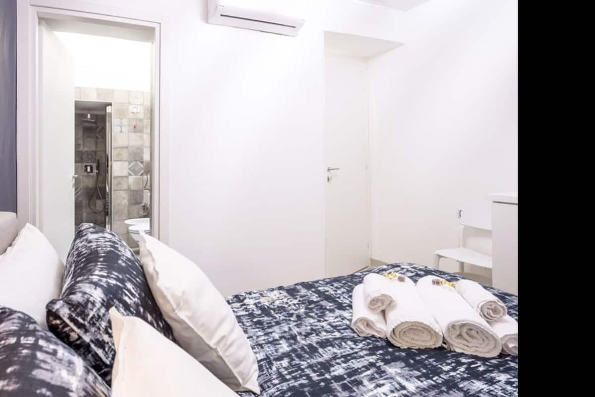 A hotel room with a bed, a bathroom with a shower, and a white wardrobe.