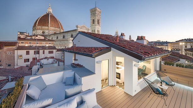 Eine Dachterrasse mit einem modernen Außenbereich zum Sitzen, Blick auf historische Gebäude und einer Kuppel im Hintergrund.
