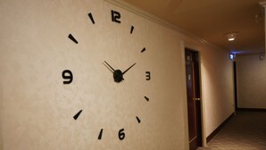 A hallway with a wall-mounted clock, a door, and a carpeted floor. - Rich Zone Hotel (Taipei)