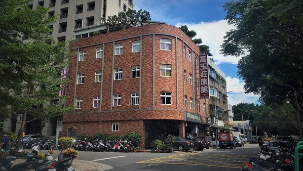 A multi-story brick building with a curved corner, featuring a sign for a hotel with a contact number. - Rich Zone Hotel (Taipei)