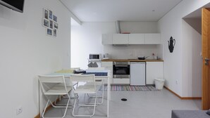 A compact kitchen with white cabinets, a microwave, a stove, and a dishwasher. There is a dining table with chairs and a small rug. - S. Thomé Apartamentos Turisticos- Ovar (Ovar)
