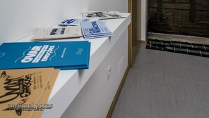 Un couloir avec un mur blanc, un miroir décoratif et une porte en bois portant un panneau indiquant la sortie de secours.