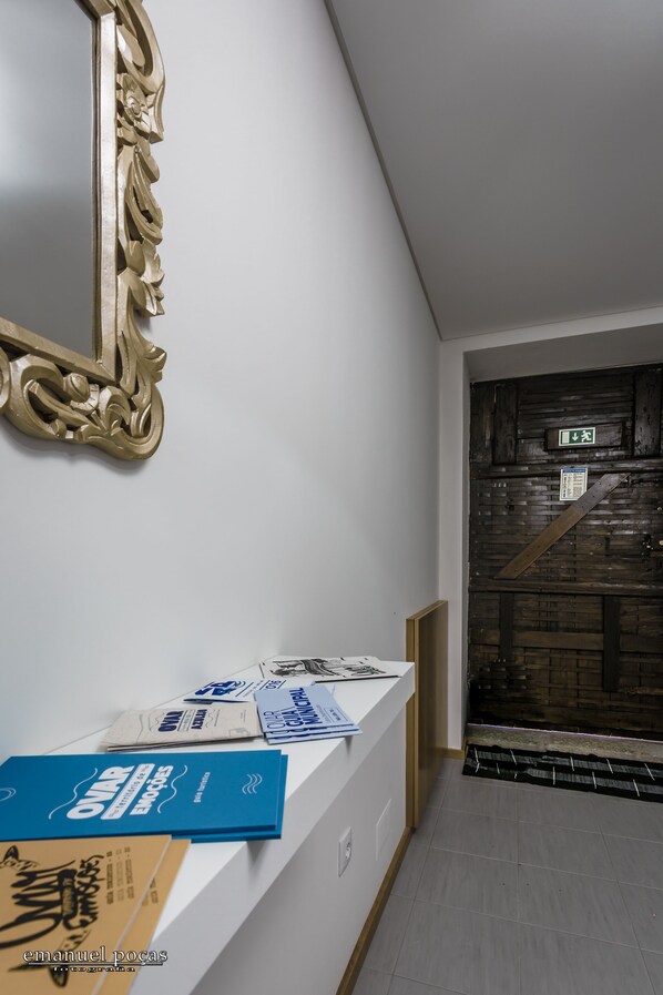 Un pasillo con pared blanca, un espejo decorativo y una puerta de madera con letrero de salida de emergencia.