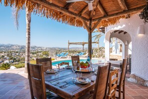 A wooden table set for dining with a view of a pool and distant landscape.
