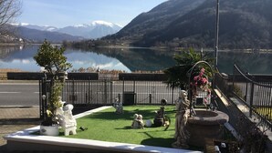 A serene lakeside park with statues, a fountain, and a clear view of snow-capped mountains.