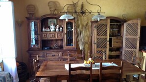 A wooden dining table with chairs, a chandelier, and a fruit bowl on the table.