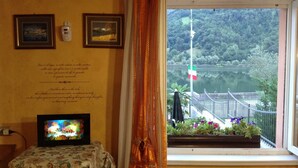 A room with a view of a lake, a table with a floral tablecloth, and two framed pictures on the wall.