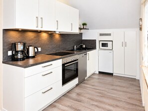 Une cuisine moderne avec des meubles blancs, un plan de travail noir, des appareils en acier inoxydable et un plancher en bois.