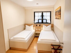 Ein Zimmer mit zwei Einzelbetten, einem fenster mit Vorhängen, einem Bild an der Wand und einem Holzboden.