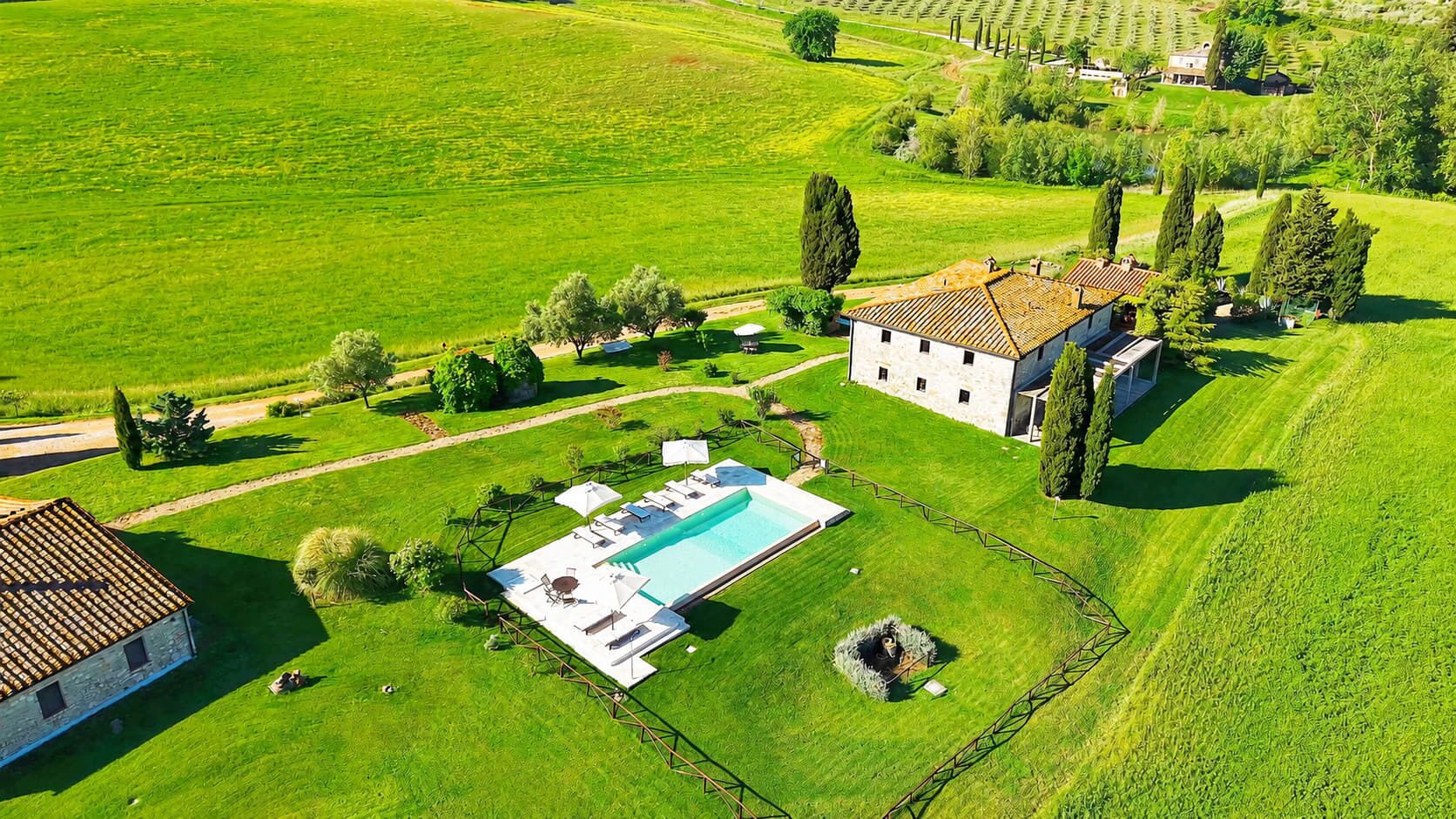 A large estate with a swimming pool, multiple buildings, and expansive green fields.