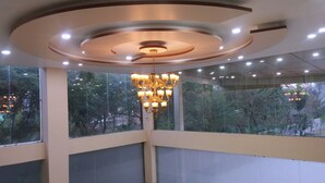 Ein Zimmer mit einer großen Kronleuchter, großen Fenstern mit Blick auf Bäume und einem modernen Deckenstil.
