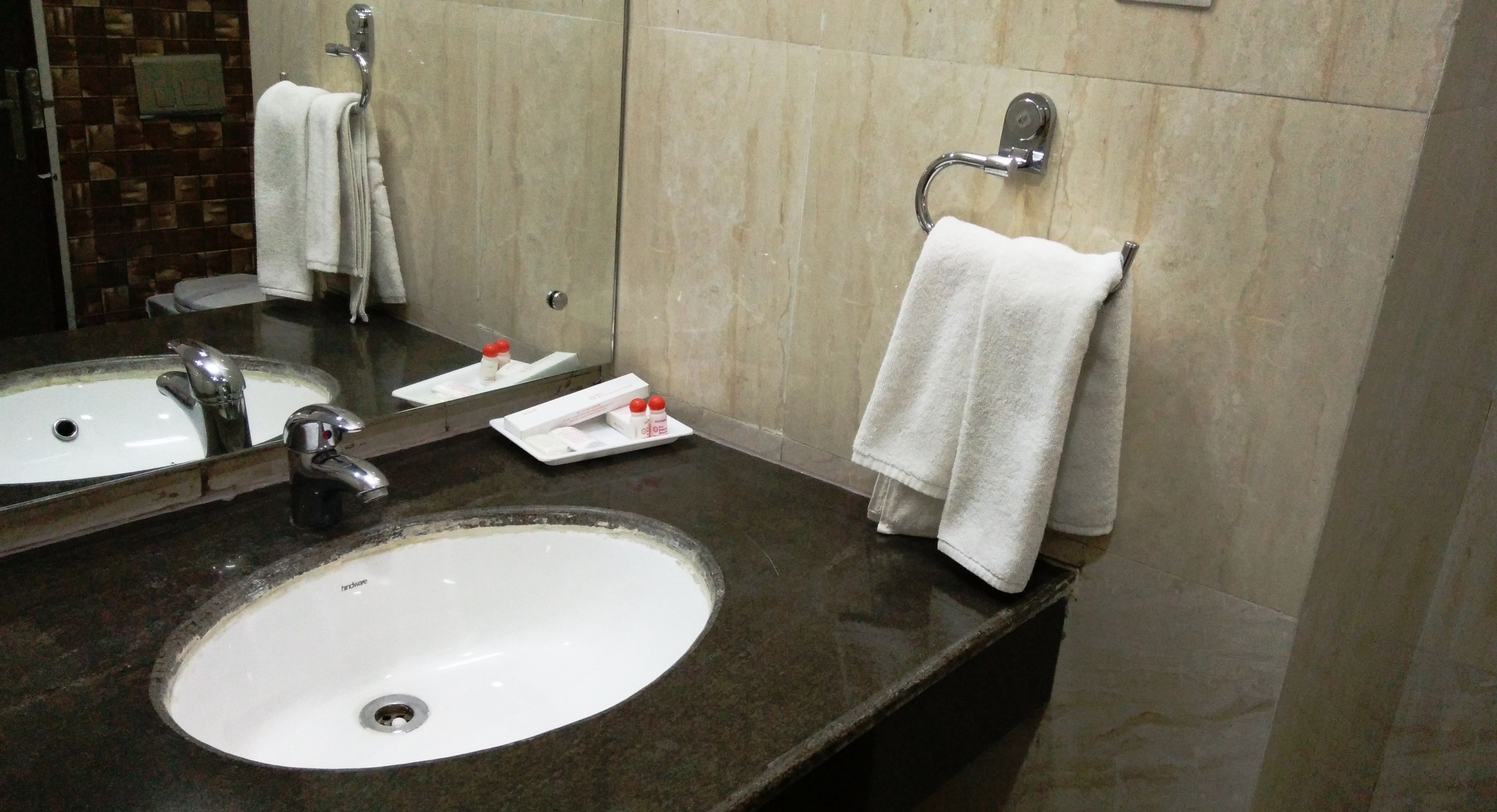A bathroom with a white sink, two mirrors, a towel rack, and a soap dispenser.