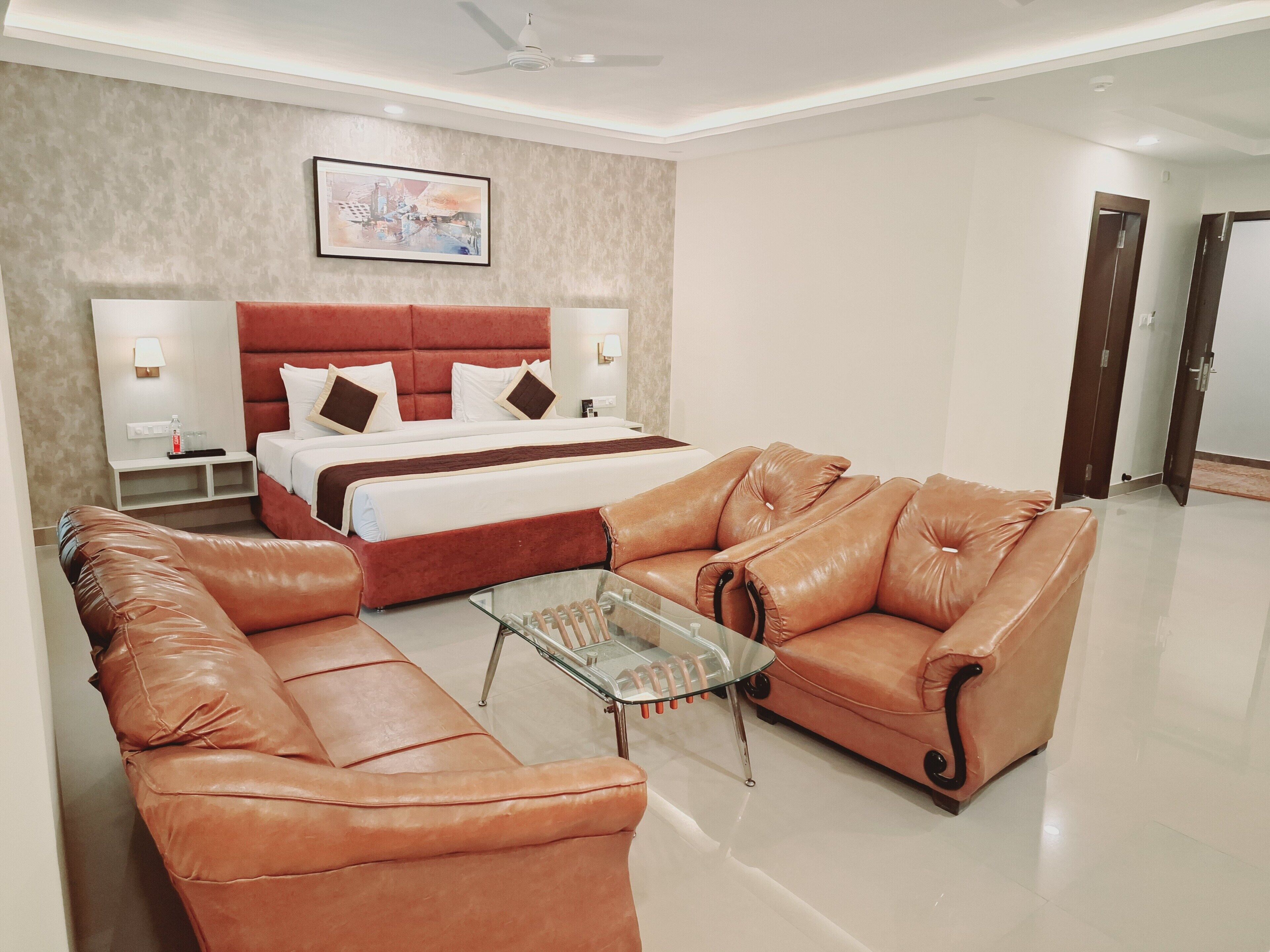 A modern hotel room with a large bed, leather sofas, a glass coffee table, and a ceiling fan.