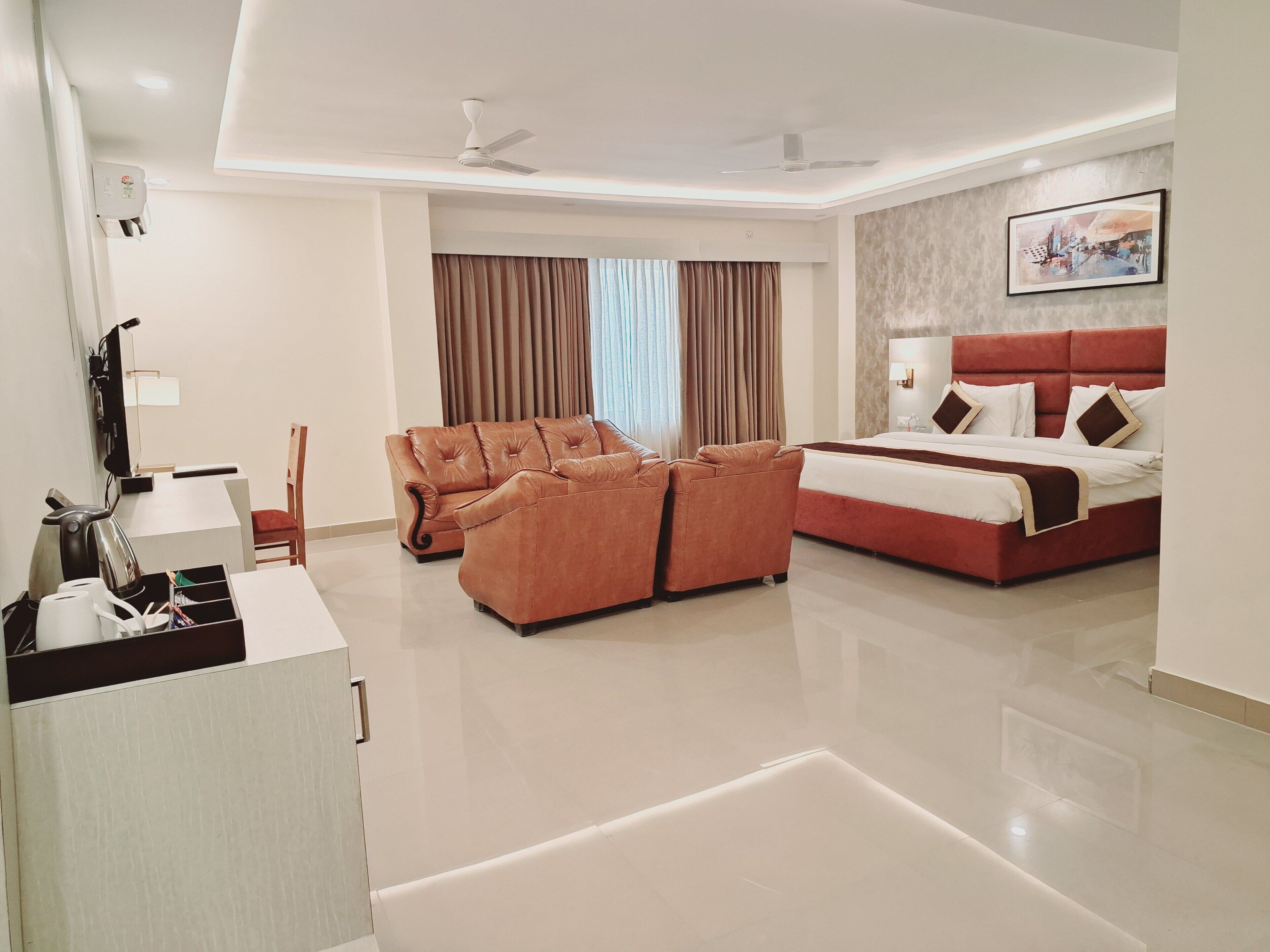 A hotel room with a bed, a sofa, a desk with a kettle, and a television.