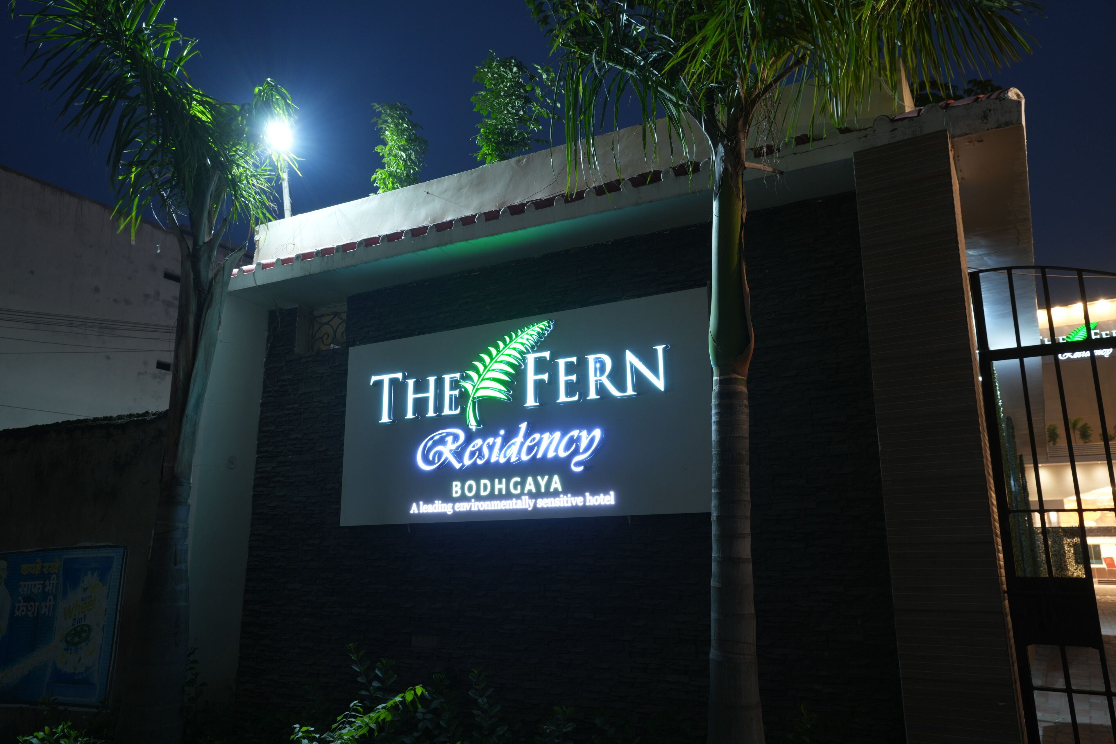 The Fern Residency, con un letrero iluminado grande, fachada de edificio moderno y entrada con portón.