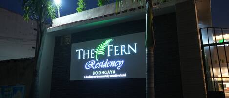 The Fern Residency, con un letrero iluminado grande, fachada de edificio moderno y entrada con portón.