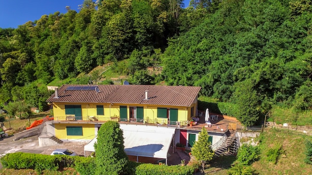A yellow building with a tiled roof, solar panels, and a balcony with outdoor seating. - Residence La Mezzaluna (Barga)