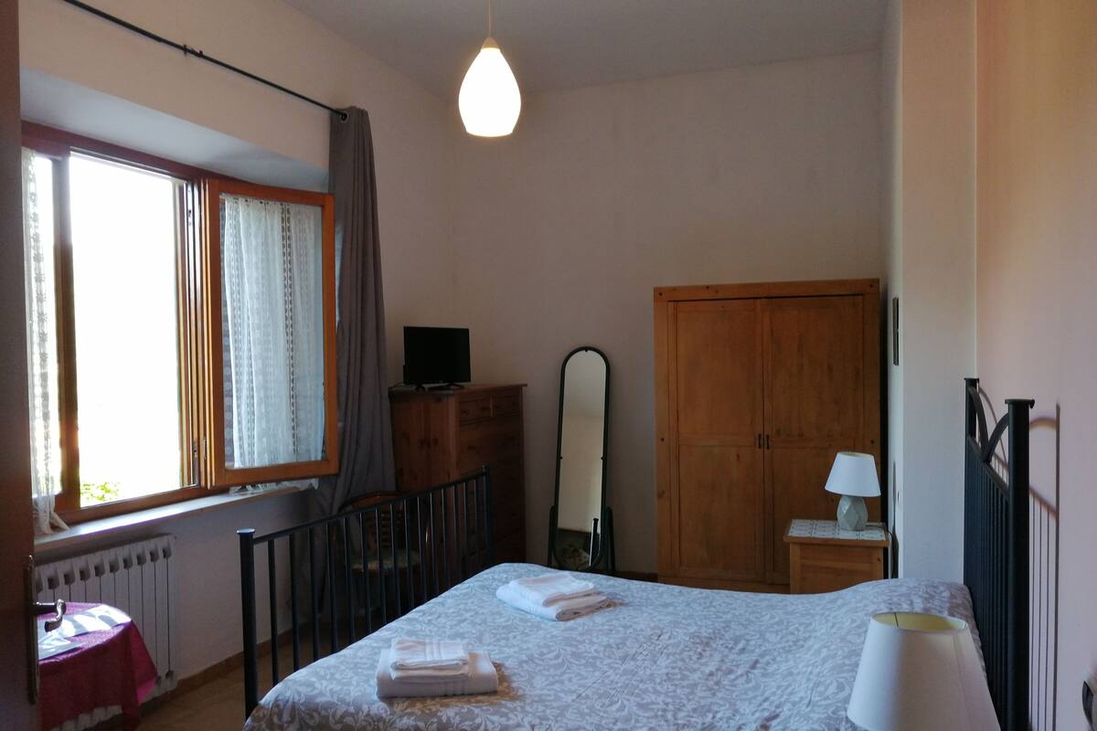 A bedroom with a bed, a dresser, a mirror, a wardrobe, and a window with curtains.