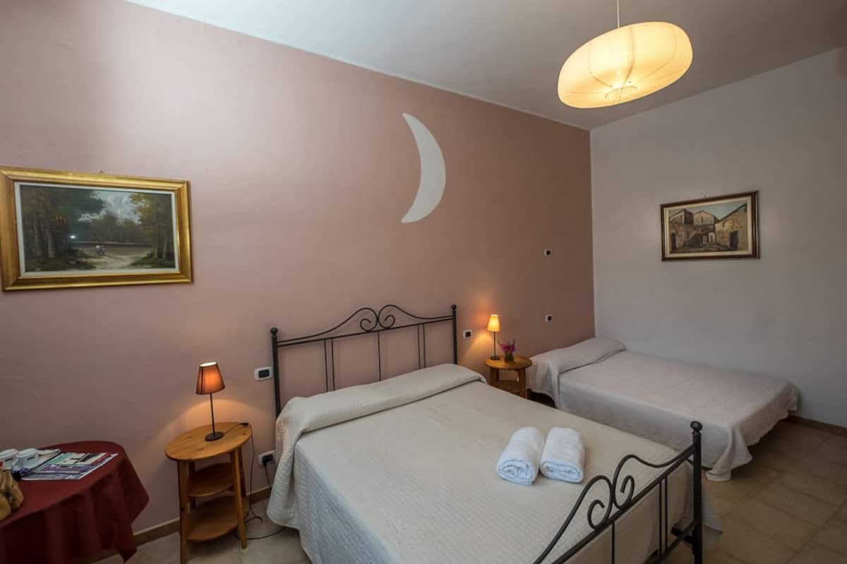 A room with two beds, a table with a red tablecloth, and a wall with a crescent moon and two framed pictures.